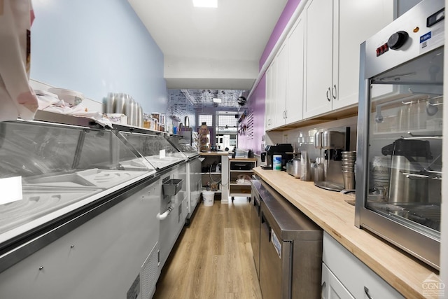 kitchen featuring wood counters, stainless steel oven, light wood-type flooring, and white cabinetry