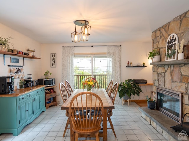 tiled dining space with a stone fireplace and a notable chandelier