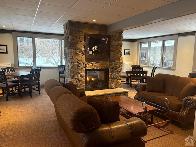 carpeted living room with a paneled ceiling, plenty of natural light, and a stone fireplace