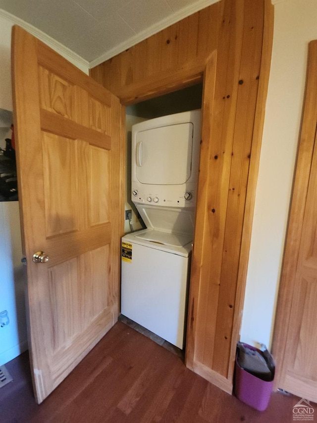 clothes washing area with dark wood-type flooring, stacked washer and dryer, ornamental molding, and wood walls