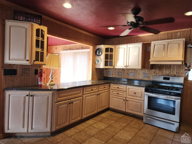 kitchen with wood walls, light tile patterned floors, ceiling fan, custom range hood, and stainless steel gas range