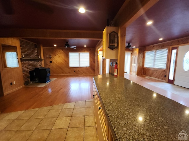 kitchen featuring ceiling fan, wooden walls, light tile patterned floors, and a wood stove