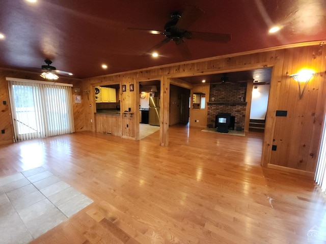 unfurnished living room with ceiling fan, ornamental molding, wooden walls, and light hardwood / wood-style floors