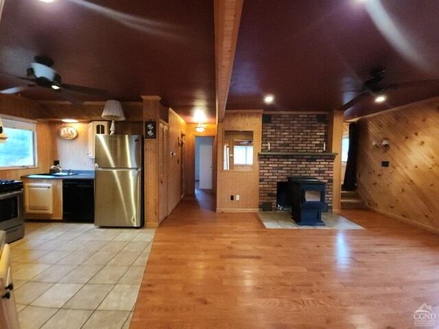 kitchen featuring appliances with stainless steel finishes, wooden walls, a wood stove, ceiling fan, and light hardwood / wood-style floors