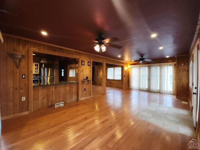 unfurnished living room featuring wood walls, plenty of natural light, and light hardwood / wood-style floors