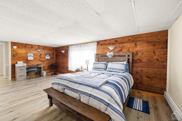 bedroom featuring wooden walls, a drop ceiling, a baseboard radiator, and light hardwood / wood-style flooring