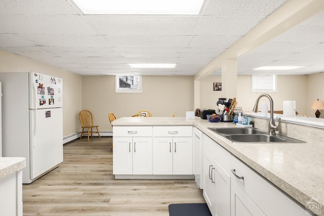 kitchen with white cabinetry, sink, kitchen peninsula, white fridge, and light wood-type flooring