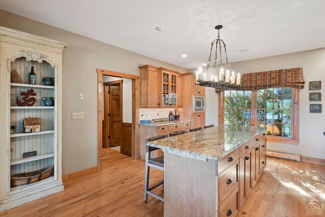 kitchen featuring light stone countertops, a kitchen island, stainless steel microwave, and light wood-type flooring