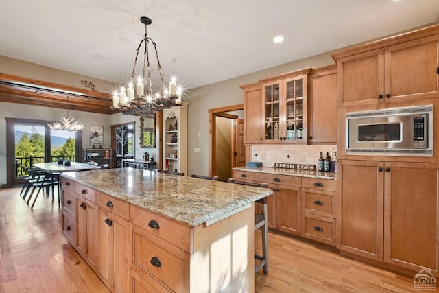 kitchen featuring a breakfast bar, stainless steel microwave, hanging light fixtures, light wood-type flooring, and a kitchen island