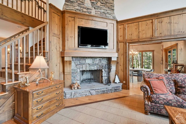 living room featuring wood walls, a stone fireplace, a high ceiling, and light hardwood / wood-style flooring