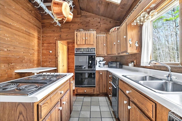 kitchen featuring dobule oven black, wood walls, stovetop with downdraft, a sink, and vaulted ceiling