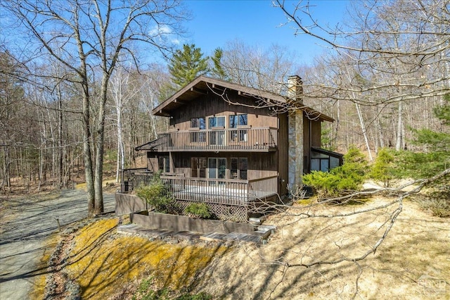 view of front facade featuring a view of trees, a wooden deck, a chimney, and a balcony