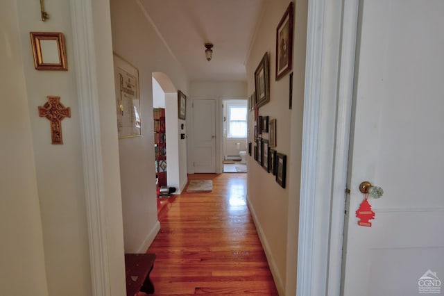 hallway featuring arched walkways, baseboards, and light wood finished floors
