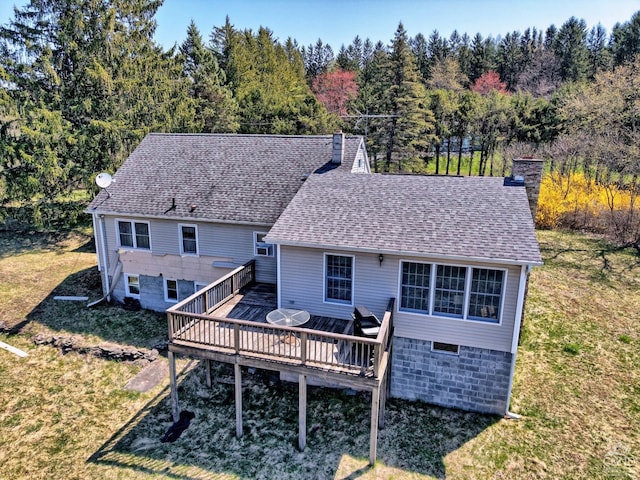 rear view of property featuring a chimney, a wooden deck, a wooded view, a yard, and a shingled roof