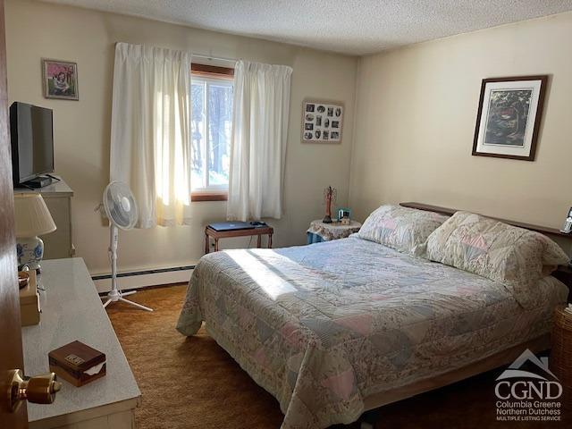 bedroom featuring a baseboard heating unit, dark carpet, and a textured ceiling