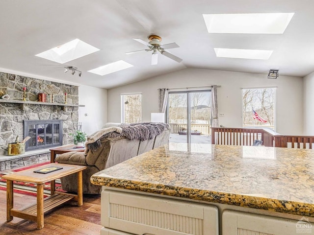 kitchen featuring lofted ceiling, cream cabinets, wood finished floors, and a stone fireplace