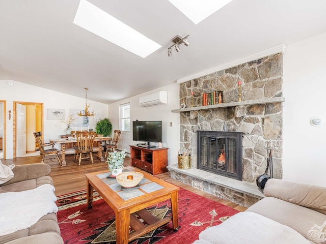 living room with vaulted ceiling with skylight, a wall unit AC, a fireplace, and wood finished floors