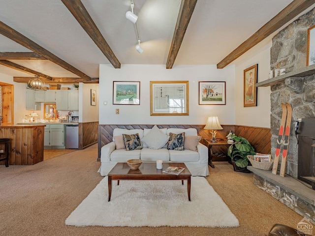 living area with light colored carpet, a wainscoted wall, a stone fireplace, wood walls, and beam ceiling