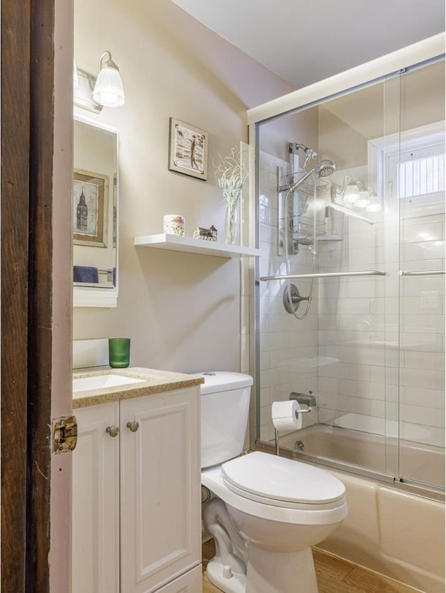 bathroom featuring wood finished floors, vanity, toilet, and bath / shower combo with glass door