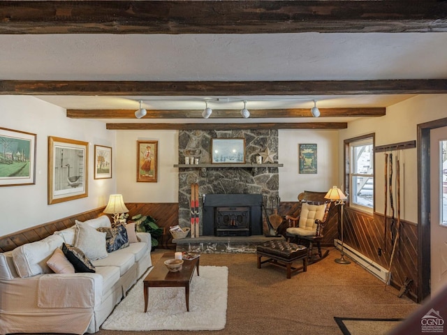 living room with a stone fireplace, a baseboard heating unit, carpet flooring, wainscoting, and beam ceiling