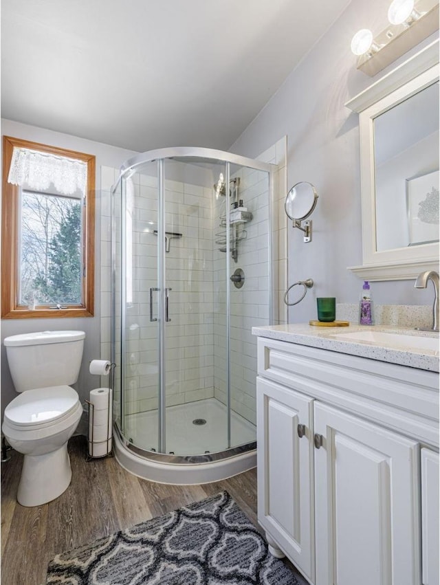 bathroom with toilet, a stall shower, wood finished floors, and vanity