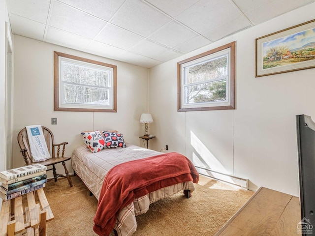 carpeted bedroom with a paneled ceiling and a baseboard heating unit