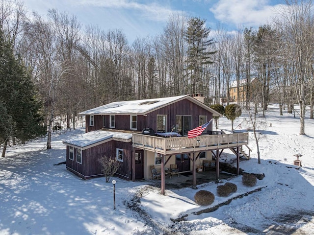 snow covered house featuring stairs, a chimney, and a wooden deck