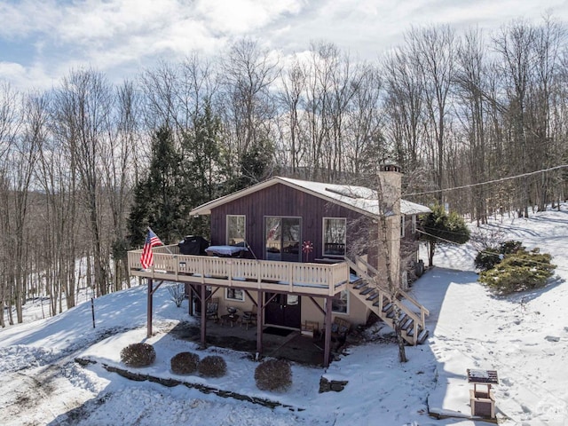 snow covered house with a chimney, stairway, and a wooden deck