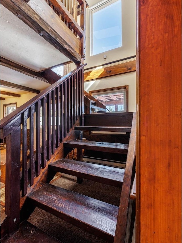 staircase featuring a healthy amount of sunlight and beamed ceiling