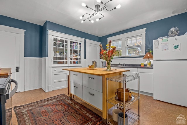 kitchen with a chandelier, white cabinets, a center island, white fridge, and butcher block counters