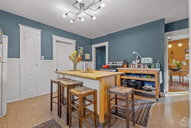 kitchen featuring a chandelier, a kitchen bar, stainless steel electric range oven, and wooden counters