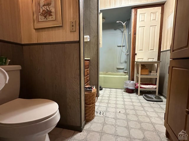 bathroom featuring toilet, wooden walls, and enclosed tub / shower combo