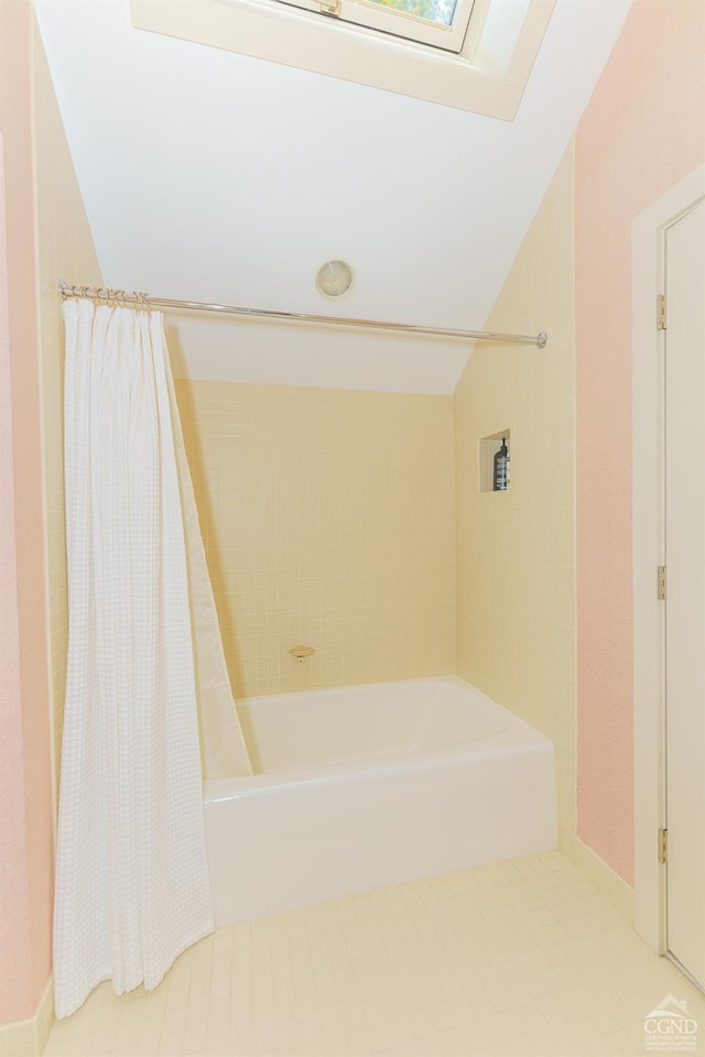 bathroom featuring lofted ceiling with skylight, tile patterned flooring, and shower / bath combination with curtain