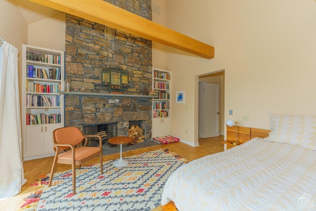 bedroom featuring a stone fireplace, a towering ceiling, and light hardwood / wood-style flooring