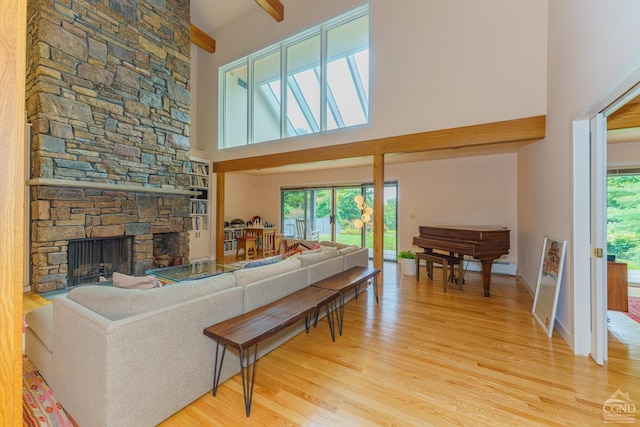 living room with beamed ceiling, a towering ceiling, light hardwood / wood-style flooring, and a stone fireplace