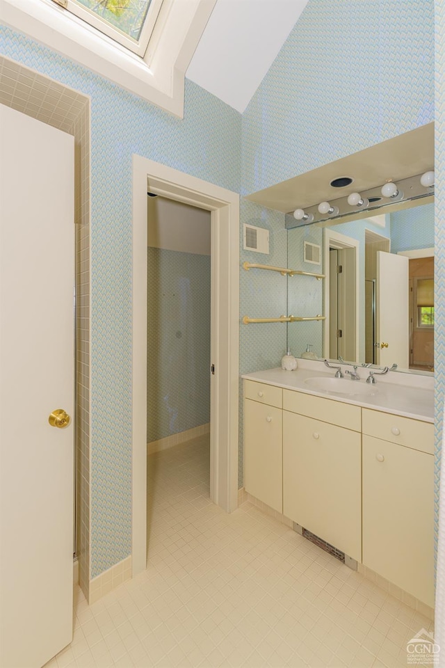 bathroom with vaulted ceiling with skylight, vanity, and tile patterned floors