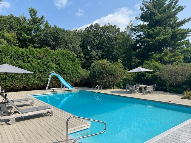 view of swimming pool with a patio area, a water slide, and a wooden deck