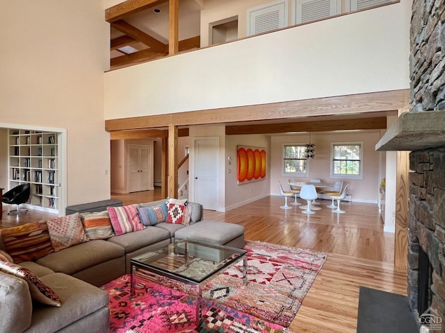 living room with beam ceiling, a stone fireplace, hardwood / wood-style floors, and a towering ceiling