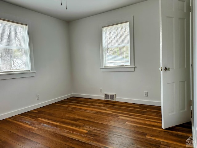 unfurnished room with dark wood-style floors, visible vents, and baseboards