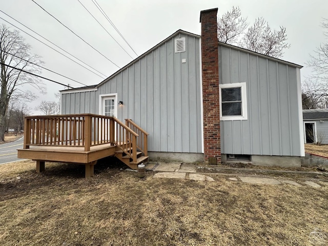 rear view of property featuring board and batten siding, a chimney, and a deck