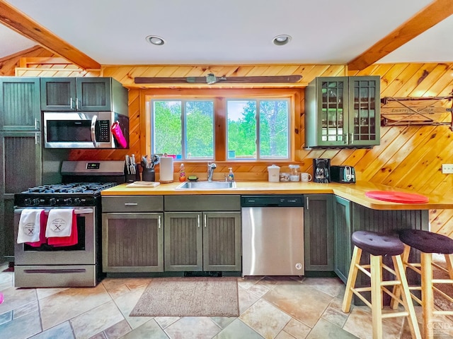 kitchen featuring wooden walls, sink, appliances with stainless steel finishes, and green cabinetry