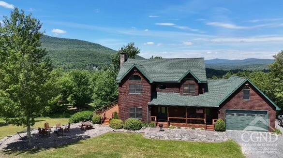 cabin with a mountain view, a front lawn, covered porch, and a garage