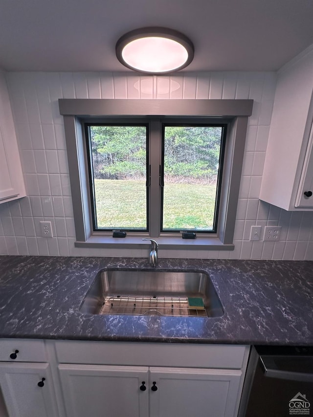 kitchen with dishwasher, dark stone countertops, a sink, white cabinetry, and backsplash