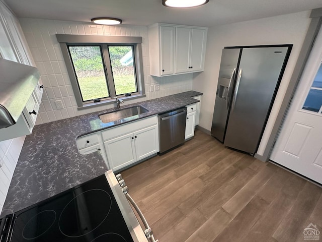 kitchen with stainless steel appliances, wood finished floors, a sink, white cabinets, and backsplash