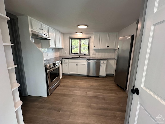 kitchen with white cabinets, dark countertops, dark wood-style flooring, stainless steel appliances, and under cabinet range hood