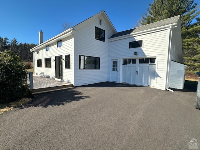 rear view of property featuring an attached garage, a deck, a chimney, and aphalt driveway