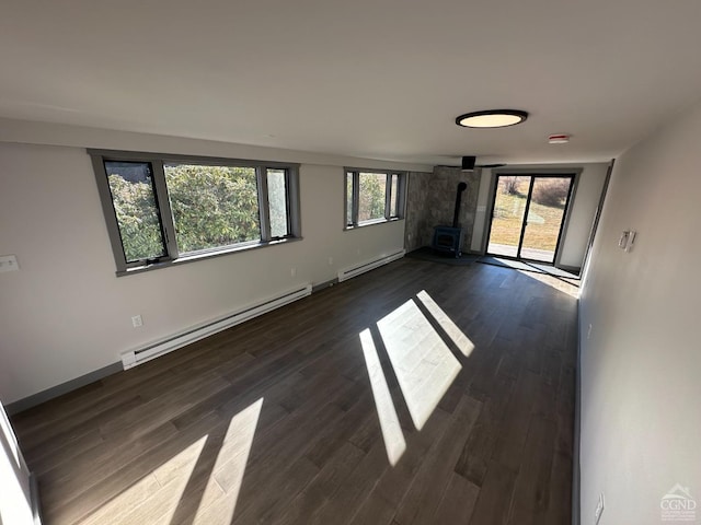 spare room featuring a wood stove, dark wood-style flooring, a baseboard radiator, and a wealth of natural light