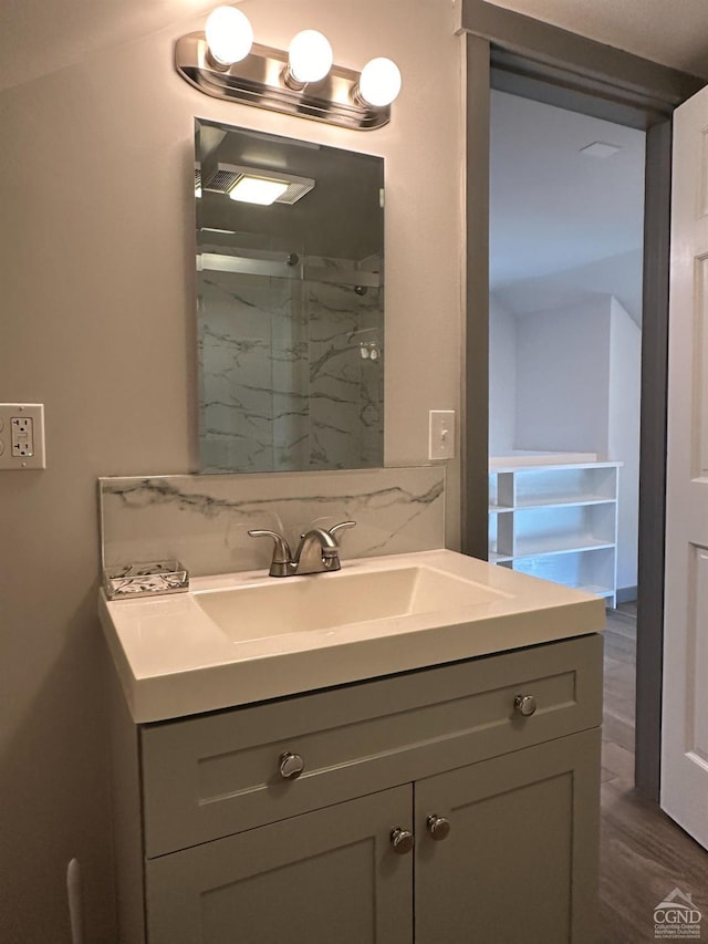 bathroom with wood finished floors, tasteful backsplash, walk in shower, and vanity