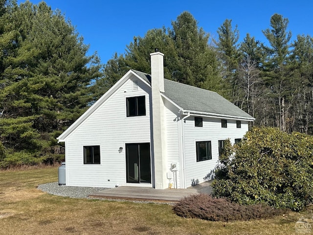 rear view of property featuring a wooden deck, a chimney, a shingled roof, and a yard