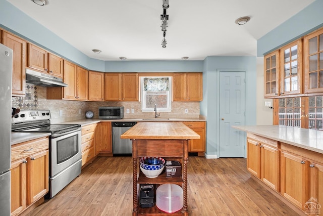 kitchen with stainless steel appliances, sink, decorative light fixtures, light hardwood / wood-style flooring, and a center island